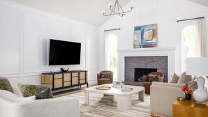 A spacious living room with a flat-screen TV, a fireplace, and a large window. - Modern, Spacious Pool Home in Plano (Plano)