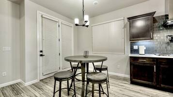 A kitchen with a round table and four stools, a dark wooden cabinet, and a light-colored tiled backsplash.