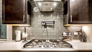 A modern kitchen with dark cabinets, a stainless steel stove, and a tiled backsplash. - Modern 3-Bedroom Villa with Jacuzzi and Gym (Las Cruces)
