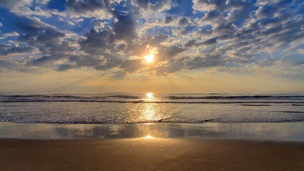 A beach with a calm sea, a clear sky, and the sun reflecting on the water. - Cozy Condo Right on the Beach! (Cocoa Beach)