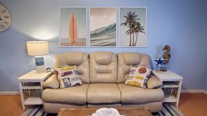 A beige leather sofa with two pillows, a starfish decoration, and a surfboard painting on the wall. - Cozy Condo Right on the Beach! (Cocoa Beach)
