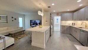 A modern kitchen with a central island, grey cabinets, stainless steel appliances, and a dining area with a white table and bench. - Mid Century Spacious House 4BR/Heated pool (Oakland Park)