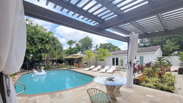 A covered outdoor swimming pool area with lounge chairs and a table. - Mid Century Spacious House 4BR/Heated pool (Oakland Park)