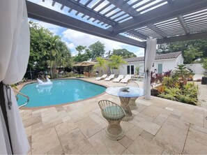 A covered outdoor swimming pool area with lounge chairs and a table. - Mid Century Spacious House 4BR/Heated pool (Oakland Park)