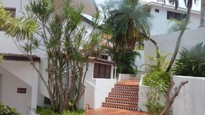 A narrow pathway leading to a staircase with a tiled floor, surrounded by lush greenery and white walls. - Cozy Golf Course View Villa inside the Wyndham Grand Rio Mar Resort (Rio Grande)