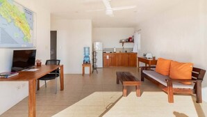 Ein großzügiger Wohnbereich mit einem Holzesstisch, einer Couch mit orangefarbenen Kissen, einer Holzbank, einem Fernseher und einer Küche im Hintergrund.