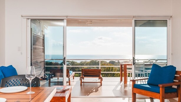 Un salon moderne doté d’une grande porte-fenêtre coulissante donnant sur un balcon avec vue sur la mer.