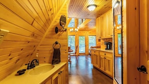 Interior de una cabaña de madera con cocina, que incluye un lavamanos, estufa y armarios.