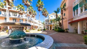 A courtyard with a central fountain, surrounded by multi-story buildings with balconies and palm trees.