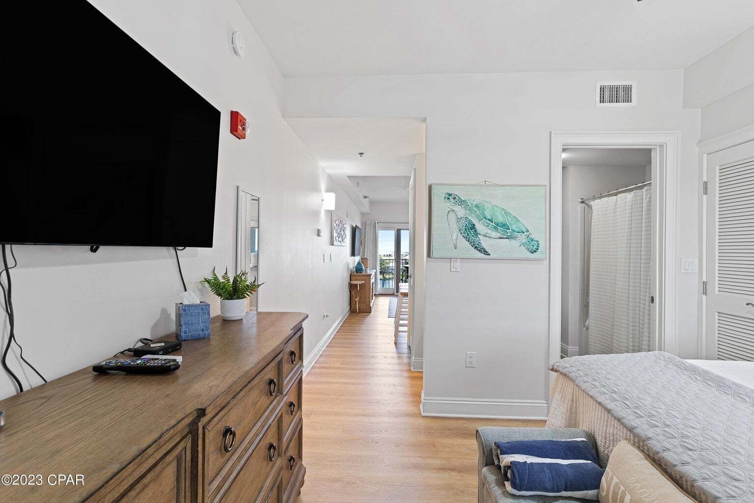 A hallway with a wooden dresser, a flat-screen TV, a potted plant, and a framed artwork of a turtle.