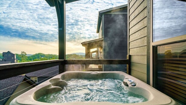 A hot tub on a balcony with a view of a house and trees. - Cozy 2BR | HOT TUB | Pets Welcome! (Sevierville)