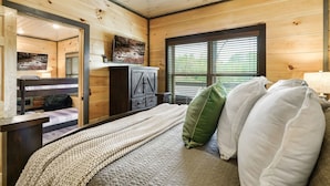 A cozy bedroom with a bed, a dresser, a mirror, and a window with blinds. - Cozy 2BR | HOT TUB | Pets Welcome! (Sevierville)