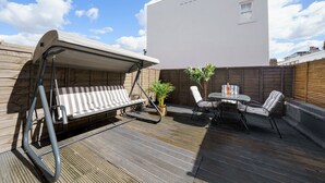 Un espacio al aire libre techado con sillón colgante, una mesita con sillas y una planta en maceta.