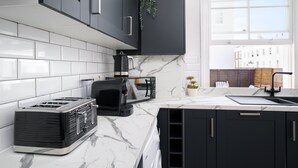 Una cocina moderna con gabinetes negros, encimera de mármol, un tostador, una cafetera y una ventana con vistas a edificios.