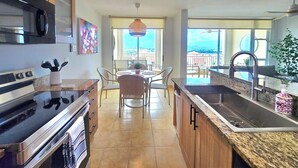 Een moderne keuken met een centraal eiland, een zithoek met stoelen en een uitzicht op de stad door grote ramen.