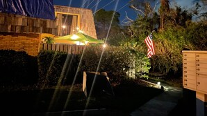 Un edificio de madera con un patio techado, una bandera estadounidense y un pequeño jardín con un sendero.