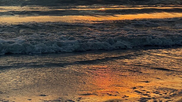 Un atardecer sobre el océano con olas acercándose a la orilla.