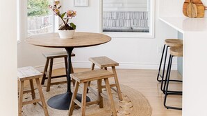Un comedor con una mesa redonda de madera, dos taburetes, un tapete tejido y una lámpara colgante.