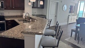 A modern kitchen with granite countertops, dark wooden cabinets, and pendant lighting. - MVG 1512 Oceanfront, Penthouse (North Myrtle Beach)