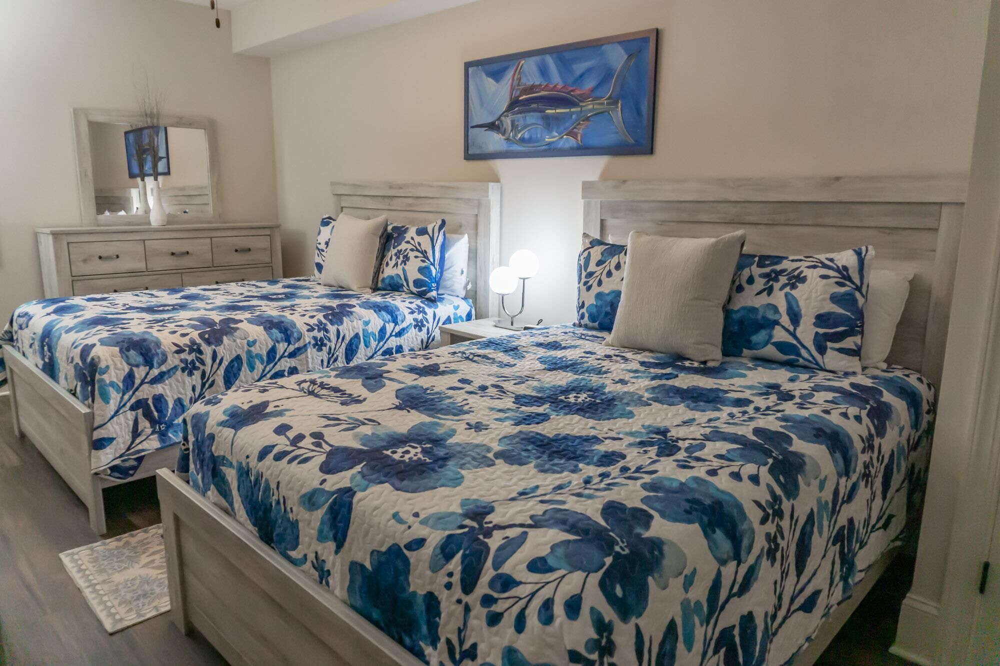 Une chambre avec deux lits, chacun agrémenté de draps à motifs floraux, une table de chevet avec une lampe et un tableau accroché au mur.