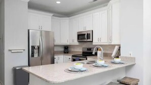 A modern kitchen with white cabinets, stainless steel appliances, and a granite countertop. - Charleston’s Folly! King Suite - Walk to Center St (Charleston)