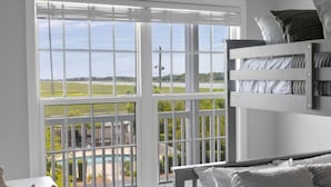 A bedroom with a bunk bed, large windows with a view of a pool and greenery, and a white interior. - Charleston’s Folly! King Suite - Walk to Center St (Charleston)