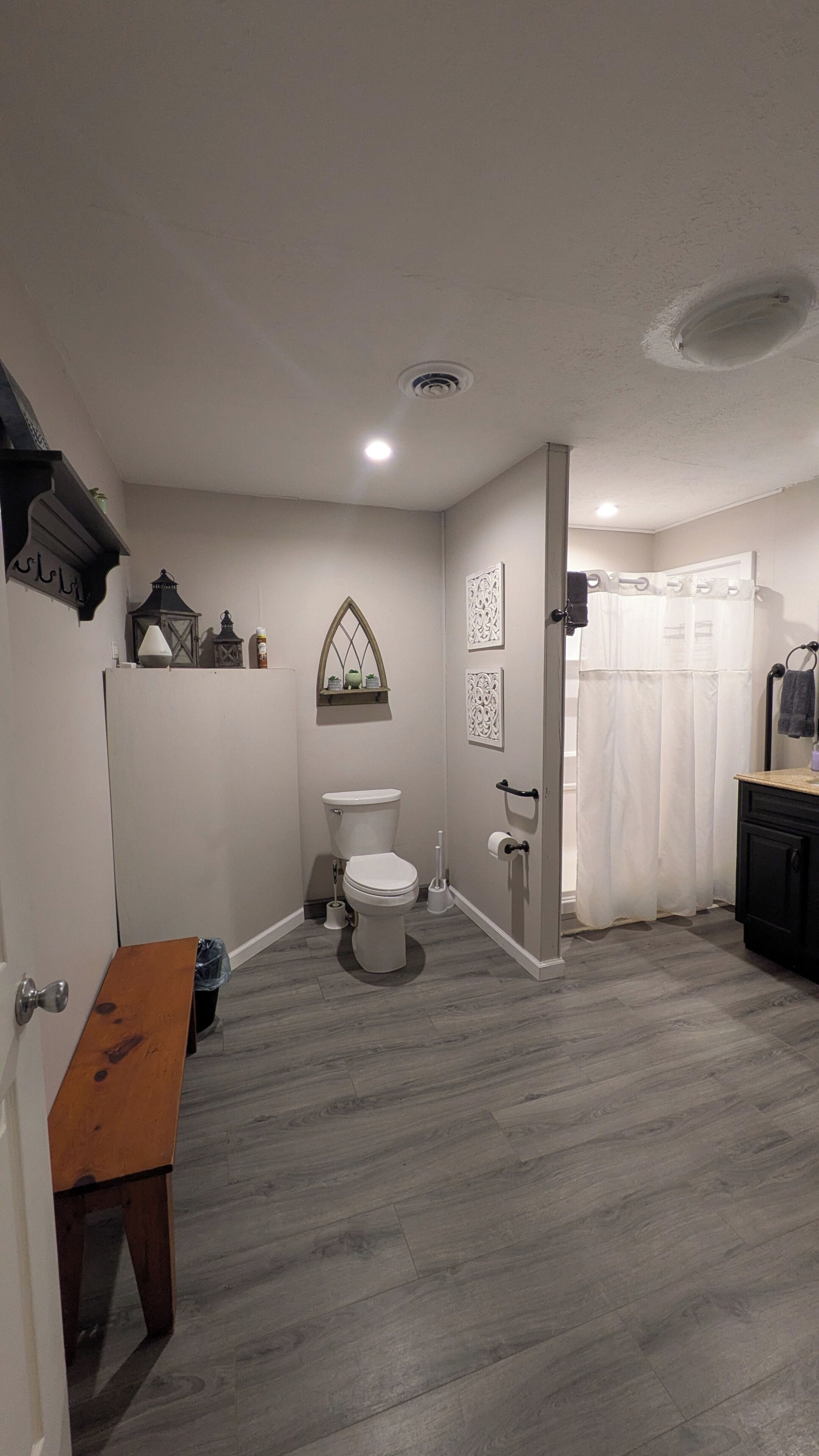 A bathroom with a toilet, shower curtain, and a wooden bench.