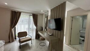Une chambre d’hôtel comprenant un lit, un bureau avec une chaise, une télévision et une salle de bain visible à travers une porte en verre.