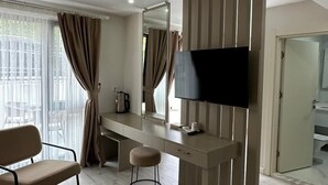 Une chambre d’hôtel moderne avec un bureau en bois, un téléviseur à écran plat, un fauteuil confortable et un petit tabouret.