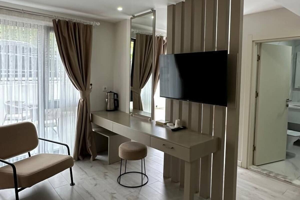 Una habitación de hotel moderna con un escritorio de madera, un televisor de pantalla plana, un sillón cómodo y un taburete pequeño.