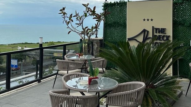 Une terrasse extérieure avec des tables rondes et des chaises en osier, donnant sur une étendue d’eau.