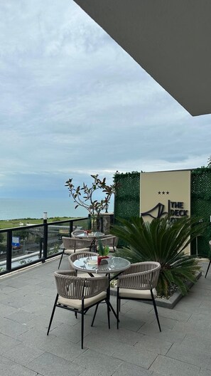An outdoor patio with round tables and wicker chairs, overlooking a body of water. - The Deck Otel (Trabzon)