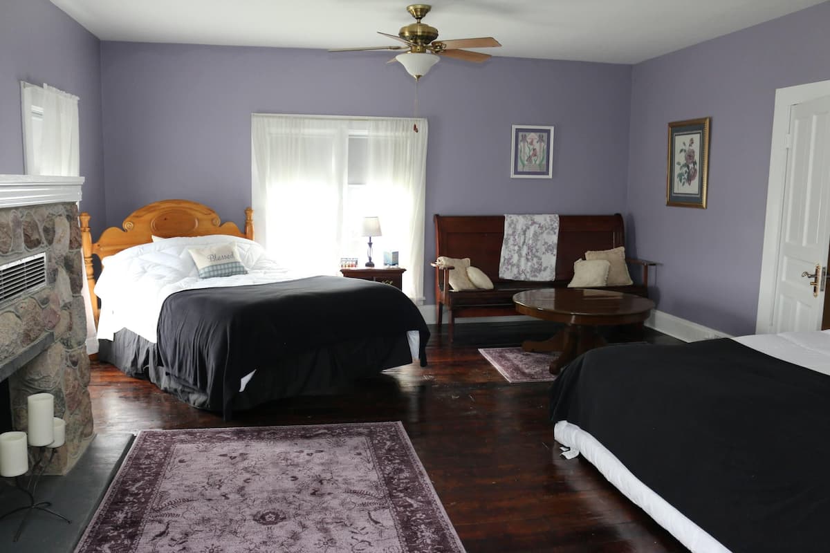 Une chambre avec deux lits, une cheminée, une table ronde et un ventilateur de plafond.