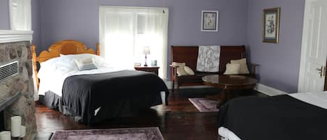 A bedroom with two beds, a fireplace, a round table, and a ceiling fan.