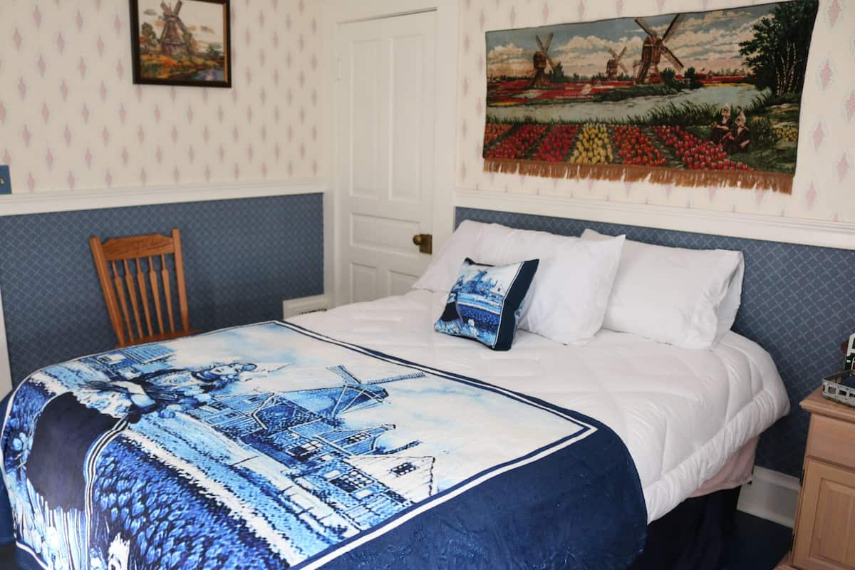 Une chambre à coucher avec un lit, une chaise en bois, une table de chevet et un tableau accroché au mur.