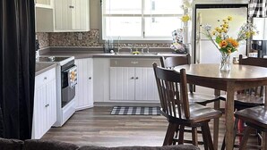 Een praktische keuken met witte kasten, een eethoek met een houten tafel en stoelen, en een groot raam dat voor natuurlijk licht zorgt.