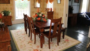 Een eetkamer met een houten tafel en stoelen, een bloemenkleed en een raam met gordijnen.