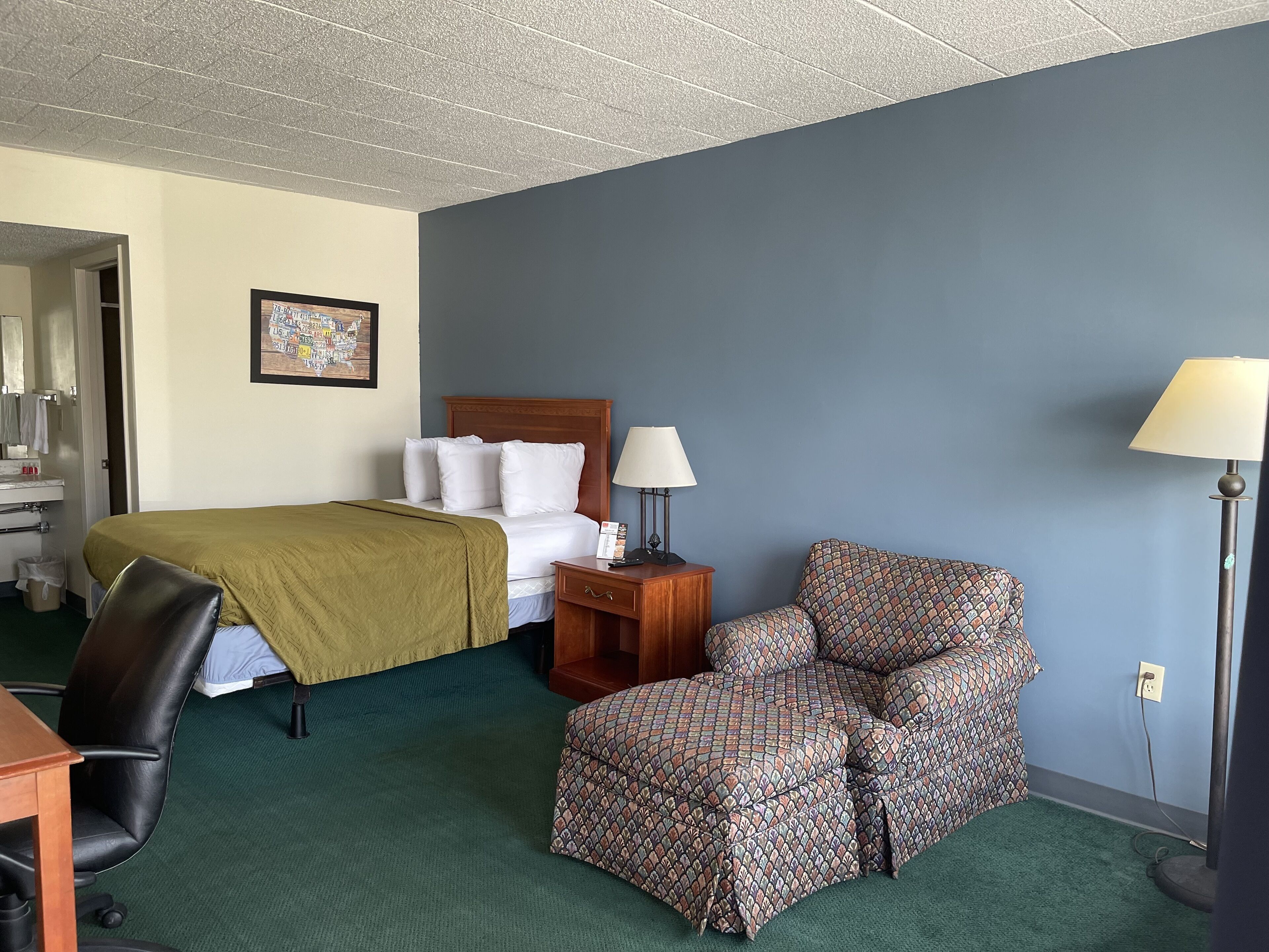 A hotel room with a bed, a desk, a chair, a lamp, and a picture on the wall.