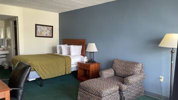 A hotel room with a bed, a desk, a chair, a lamp, and a picture on the wall.