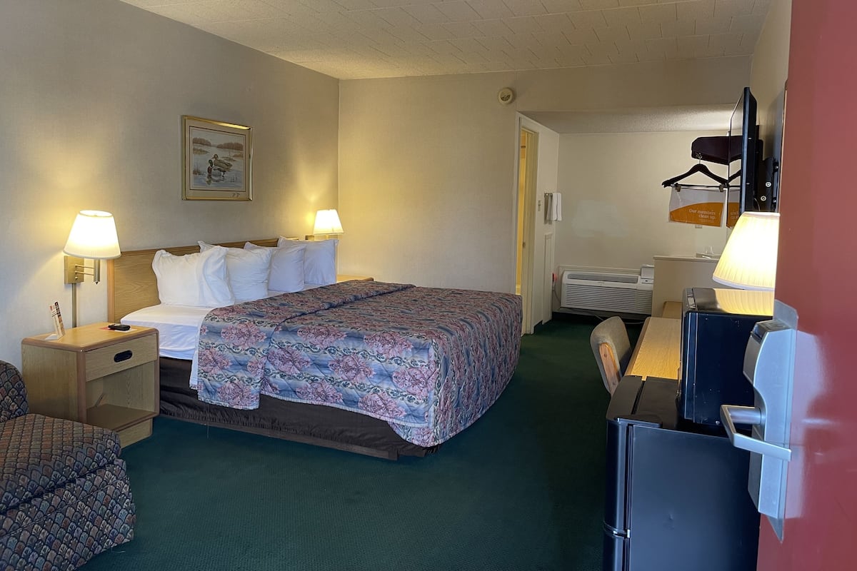 A hotel room with a bed, two bedside lamps, a chair, a desk, and a coat rack.