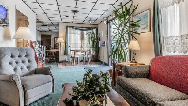 Una sala de estar acogedora con un sofá gris, un sofá rojo y una mesa de centro con una planta. Se observa un comedor con una mesa y sillas al fondo.