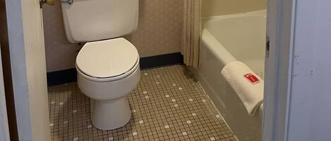 A small bathroom with a toilet, a towel rack with two towels, a shower curtain, and a tiled floor.