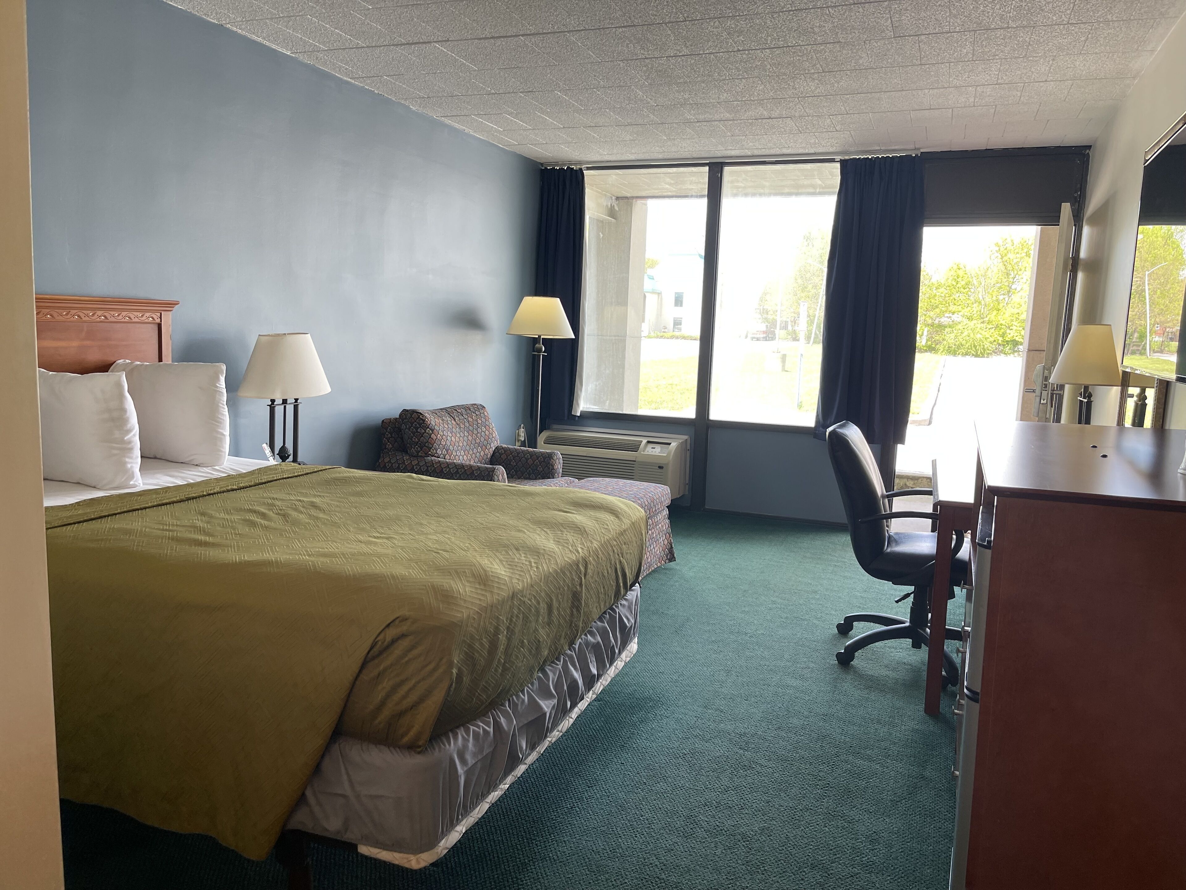 A hotel room with a bed, desk, chair, and large windows.