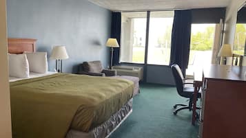 A hotel room with a bed, desk, chair, and large windows.