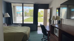 Habitación de hotel con cama, escritorio, silla, televisión y vistas al exterior.