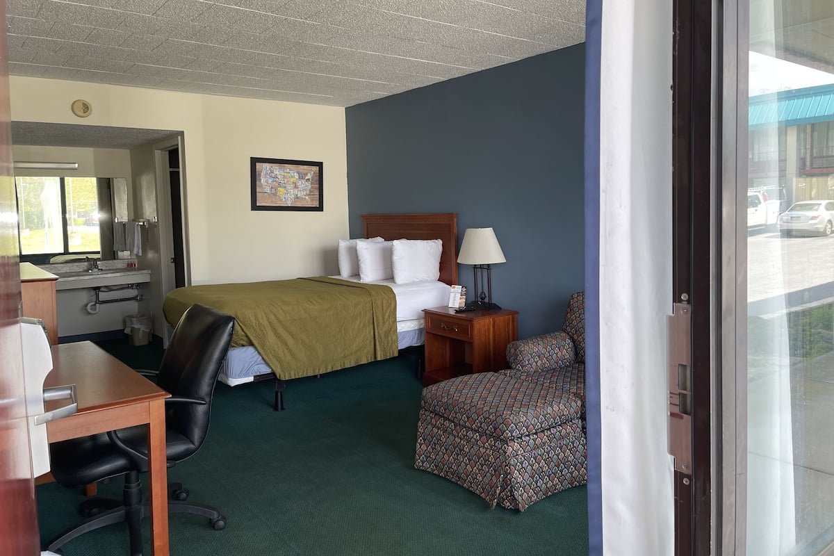 A hotel room with a bed, desk, chair, and a window with a view of the street.