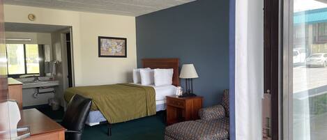 A hotel room with a bed, desk, chair, and a window with a view of the street.