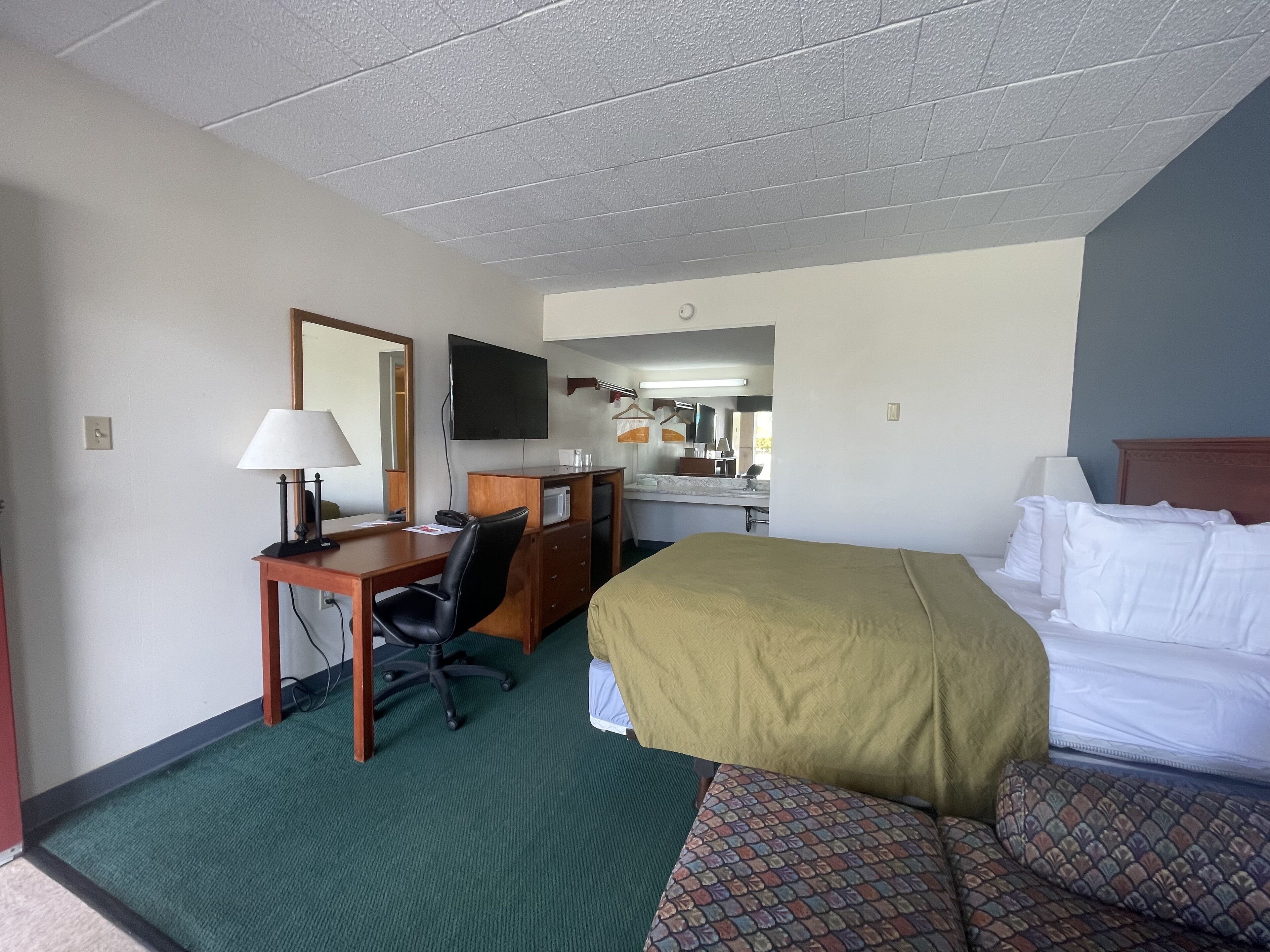 Hotelkamer met een bed, een bureau met stoel, een televisie en een badkamer zichtbaar door een geopende deur.