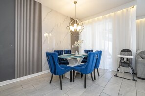 A dining area with a glass-top table, blue upholstered chairs, a chandelier, and a baby changing station. - 4832- Great Family Home near Disney, private pool, Storey Lake Resort. (Kissimmee)