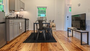 A compact kitchen with grey cabinets, a dining area with a black rug, and a TV on a stand. - Double the Fun: Two Houses, Shared Yard & Fire Pit (Kingston)